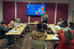 Karen Ramsey presenting to GCT Class 1 Woman standing at the front of a room teaching to students seated around tables.